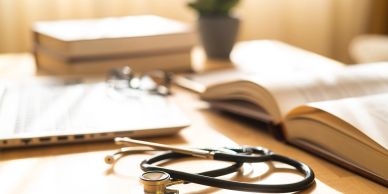 Stethoscope with books and laptop on desk.