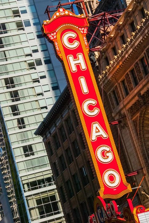 The Chicago sign illuminates the urban landscape, drawing attention from pedestrians and vehicles alike. Surrounded by towering buildings, it captures the essence of city life during a sunny midday, inviting exploration and adventure.