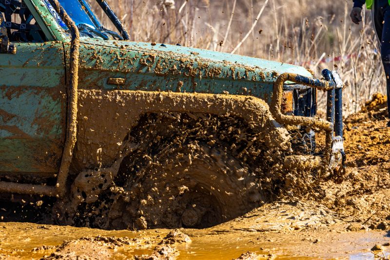 Green off-road vehicle stuck in a huge hole with mud and water, crossing difficult terrain by car, competing on the off-road race track