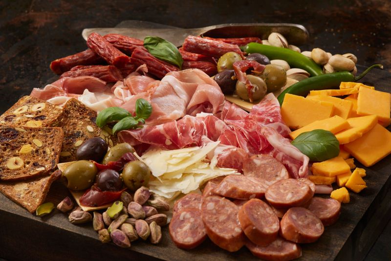 Charcuterie Board with: Prosciutto, Garlic Sausage, Genoa Salami, Pepperoni Sticks Cheddar Cheese, Parmesan, Olives, Crackers and Pistachios