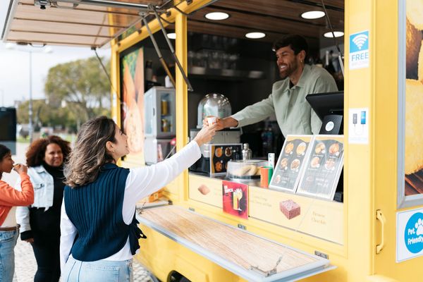 Two women smiling behind a table with coffee dispensers at an outdoor event.