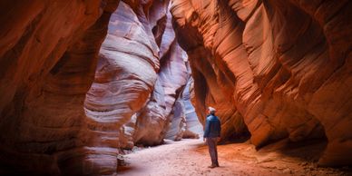 A person exploring a narrow canyon with red rock walls.