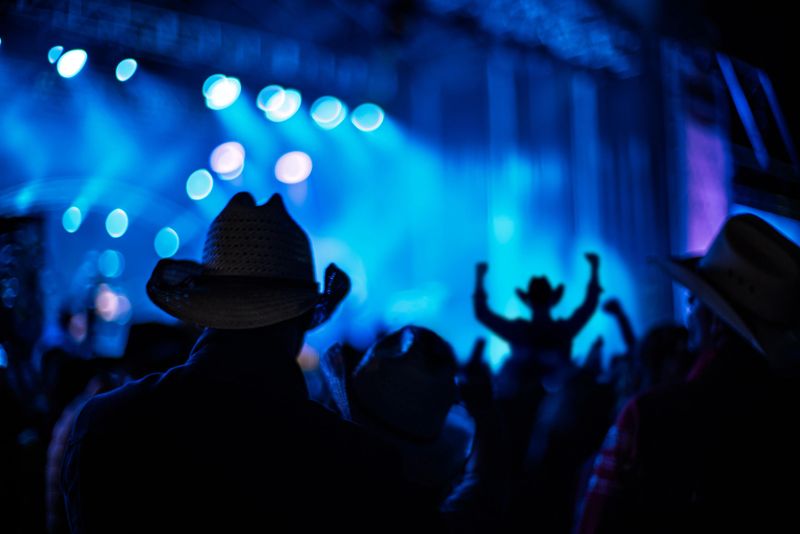 Silhouetted audience with cowboy hats at a country music concert under dynamic blue lighting.