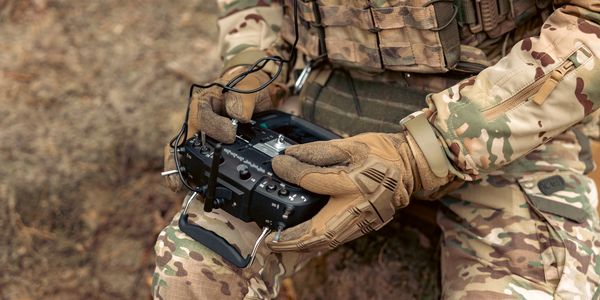 Soldier in camouflage uniform operating a remote control device outdoors.