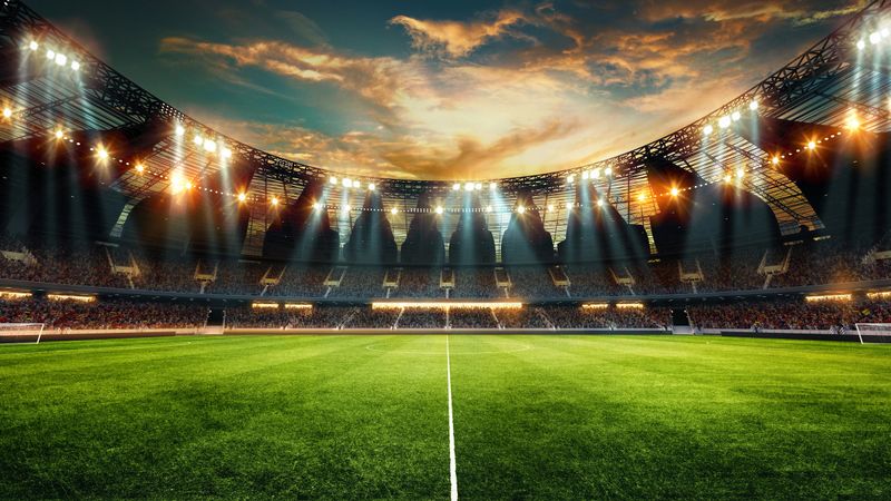 Wide-angle of modern football stadium with glass roof, bright stadium lights illuminating green field against cloudy sunset sky above. 3D render. Concept of sport event, championship, game.