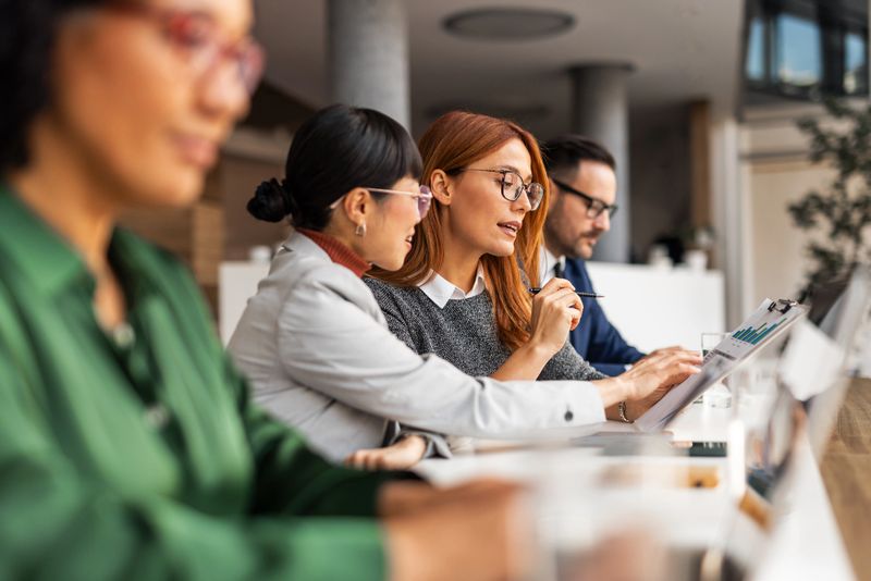 Diverse colleagues engaging in a professional discussion, analyzing documents, demonstrating teamwork in an office setting. Focus on strategy, cooperation, and communication among a business team at work.