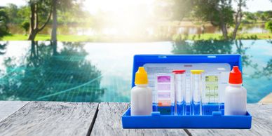 Pool water testing kit on wooden deck near a sunny pool.
