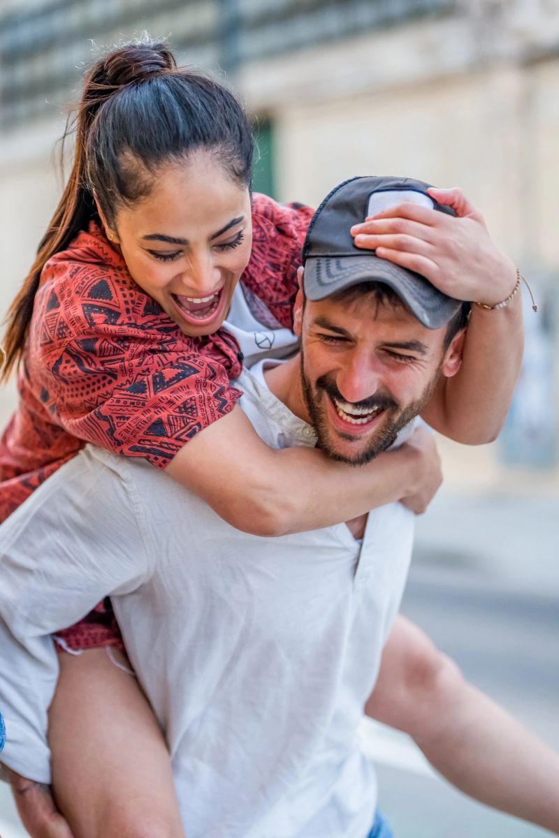 A cheerful young couple shares a joyful moment during a playful piggyback ride outdoors in the city.