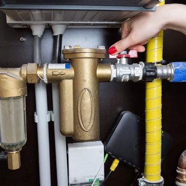 Hand adjusting a valve on a brass plumbing system under a sink.