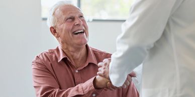 Elderly man joyfully shakes hands with a healthcare professional.