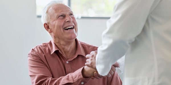 Elderly man smiling and shaking hands with a doctor.