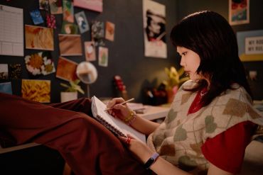 Young woman writing in a notebook in a cozy room.