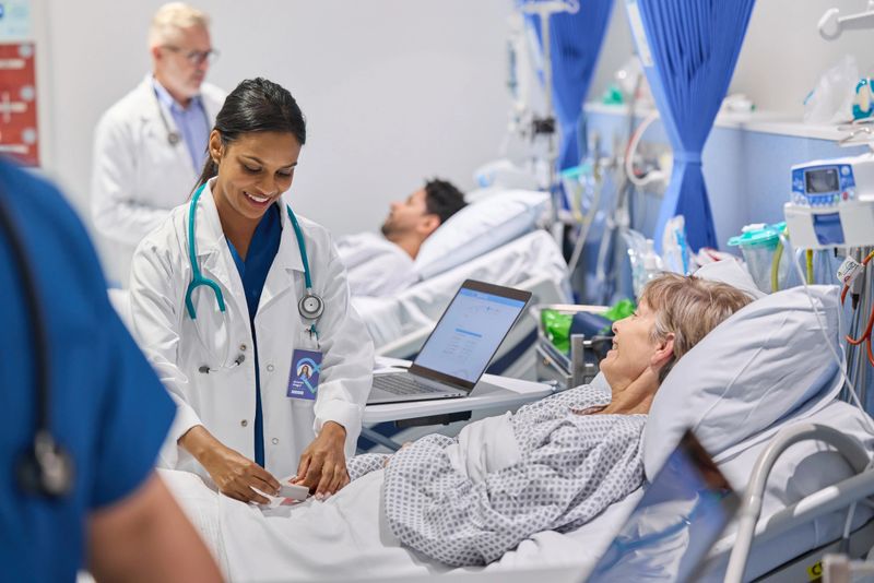Happy medical expert adjusting pulse oximeter of patient. Senior woman is smiling while reclining on gurney. She is talking with healthcare worker.