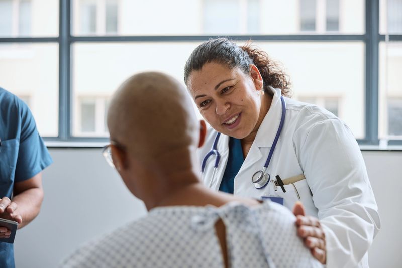 Smiling female healthcare expert consoling patient at hospital. Doctor is giving emotional support to woman. She has stethoscope around her neck.