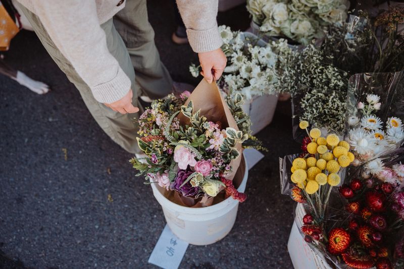 High angle view looking down at buckets of beautiful bouquets of flowers for sale at a farmer's market in San Francisco, California, USA as an unrecognizable female customer admires the flowers and chooses which she would like to buy.