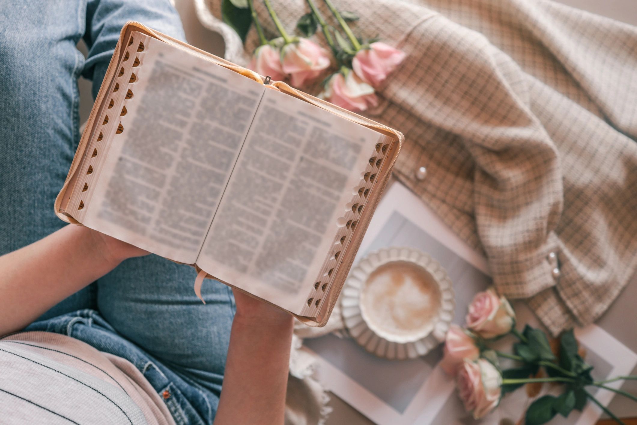 Person reading a book with flowers and coffee nearby.