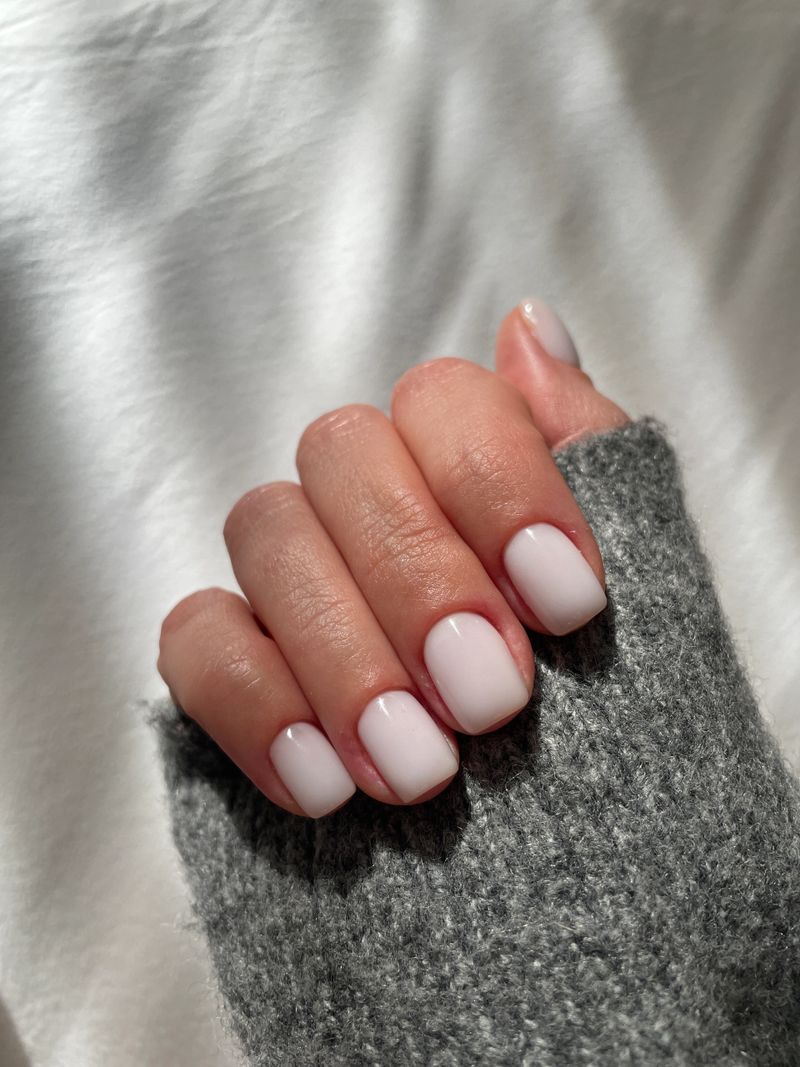 Woman's hand with fashionable milky white manicure on grey sweater