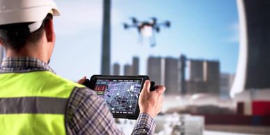 Construction worker operating a drone with a tablet at a site.