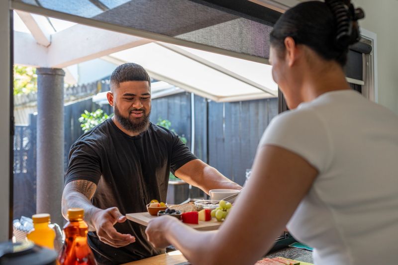 A woman hands a platter of food to a man while standing at an outdoor counter