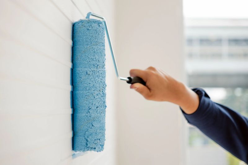 Hand holding a paint roller applying bright blue paint on a white textured wall. DIY home renovation concept, giving a fresh and modern look to interior spaces with bold color.