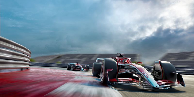 Low angle view of two racing cars taking a corner at high speed on a racetrack with empty spectators stands in the background under a stormy overcast sky.