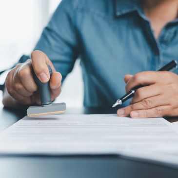Person stamping a document while holding a pen, wearing a blue shirt.