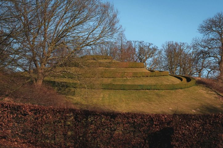 A beautifully landscaped tiered garden in Denmark shows intricate green designs under a sunny blue sky, inviting visitors to explore nature.