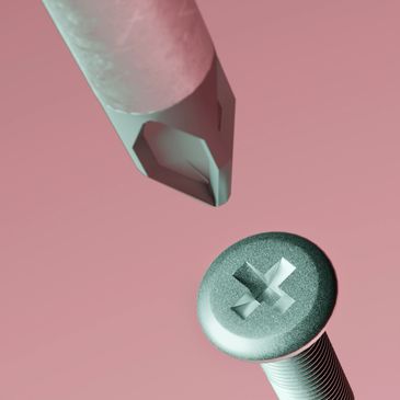 Close-up of a screwdriver tip and a screw head on a pink background.