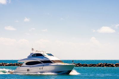 A white yacht cruising in clear blue waters near a rocky breakwater.
