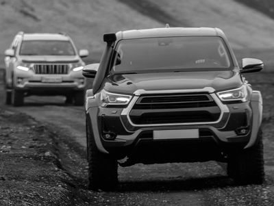Two off-road vehicles driving on a dirt path in a rugged landscape.