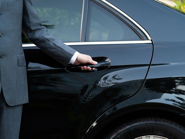 A person in a suit opening a black car door handle.