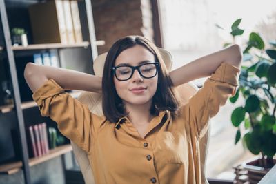 A woman with glasses relaxes in an office chair with eyes closed.