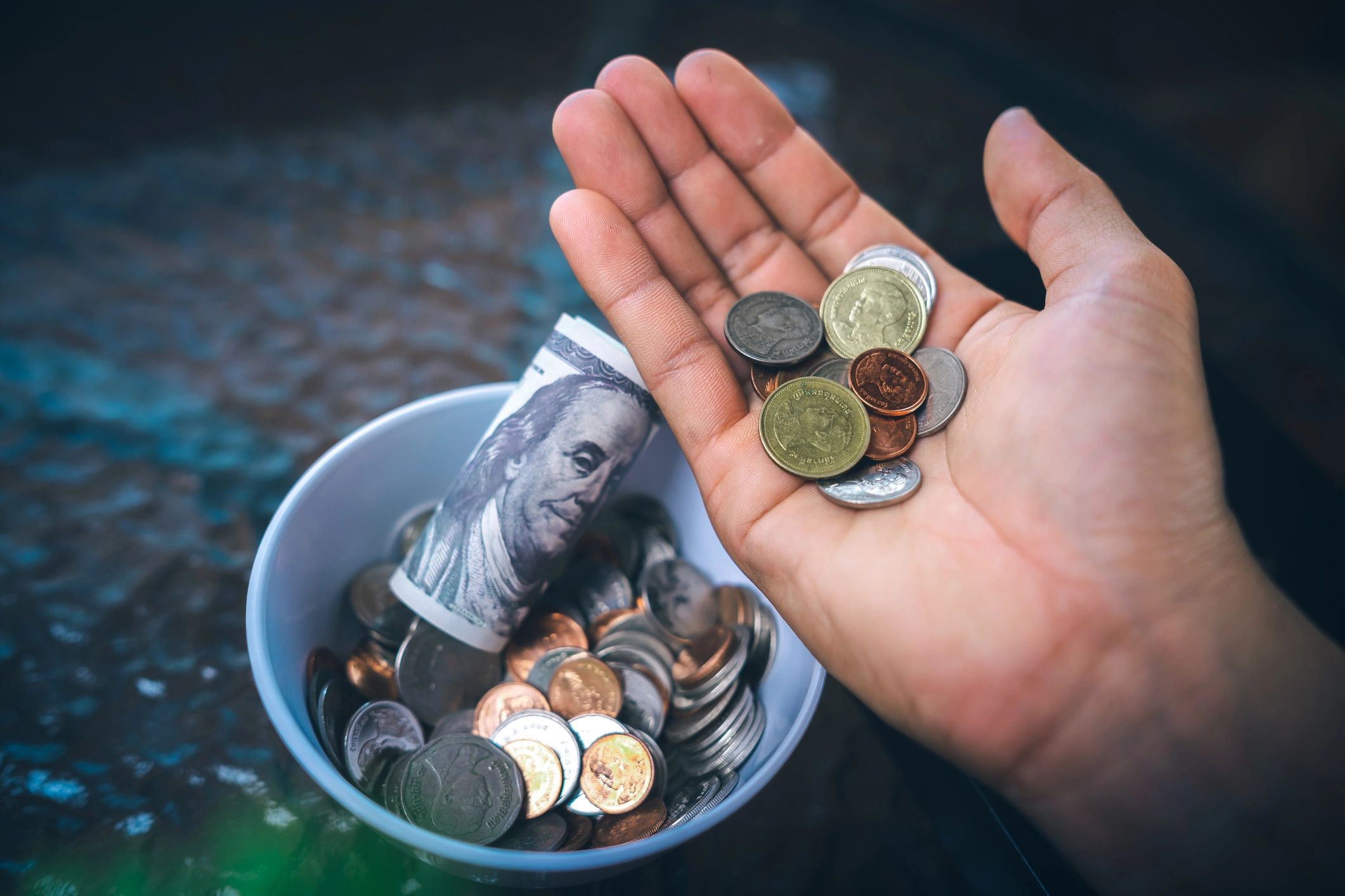Hand holding mixed coins with jar of money.