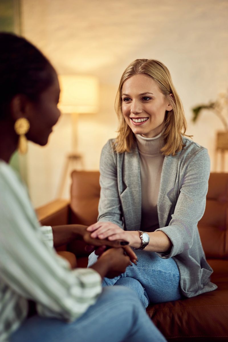Two women talking and sharing support in a warm, welcoming living room environment.