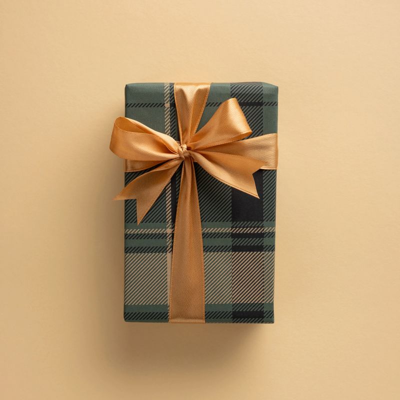 A square beautifully wrapped plaid gift box tied with a gold ribbon on a beige background