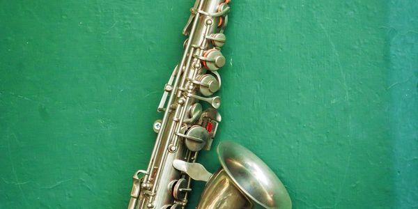 A silver saxophone resting against a green wall.