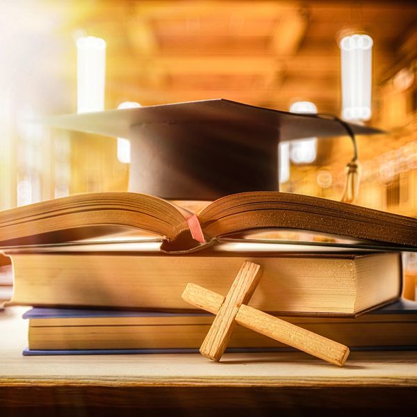 Graduation cap, books, and wooden cross on table.