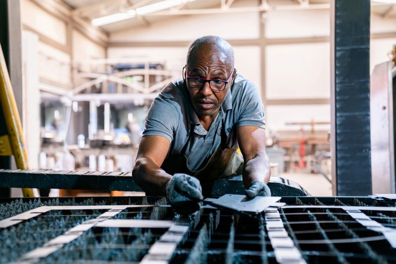Latin American metal worker operating a laser cutter and removing the debris of a sheet while working at a factory