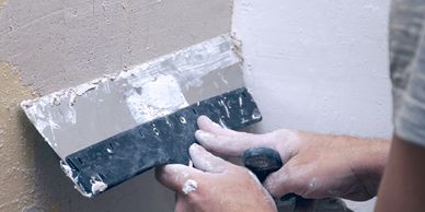 Person applying plaster to a wall with a putty knife.
