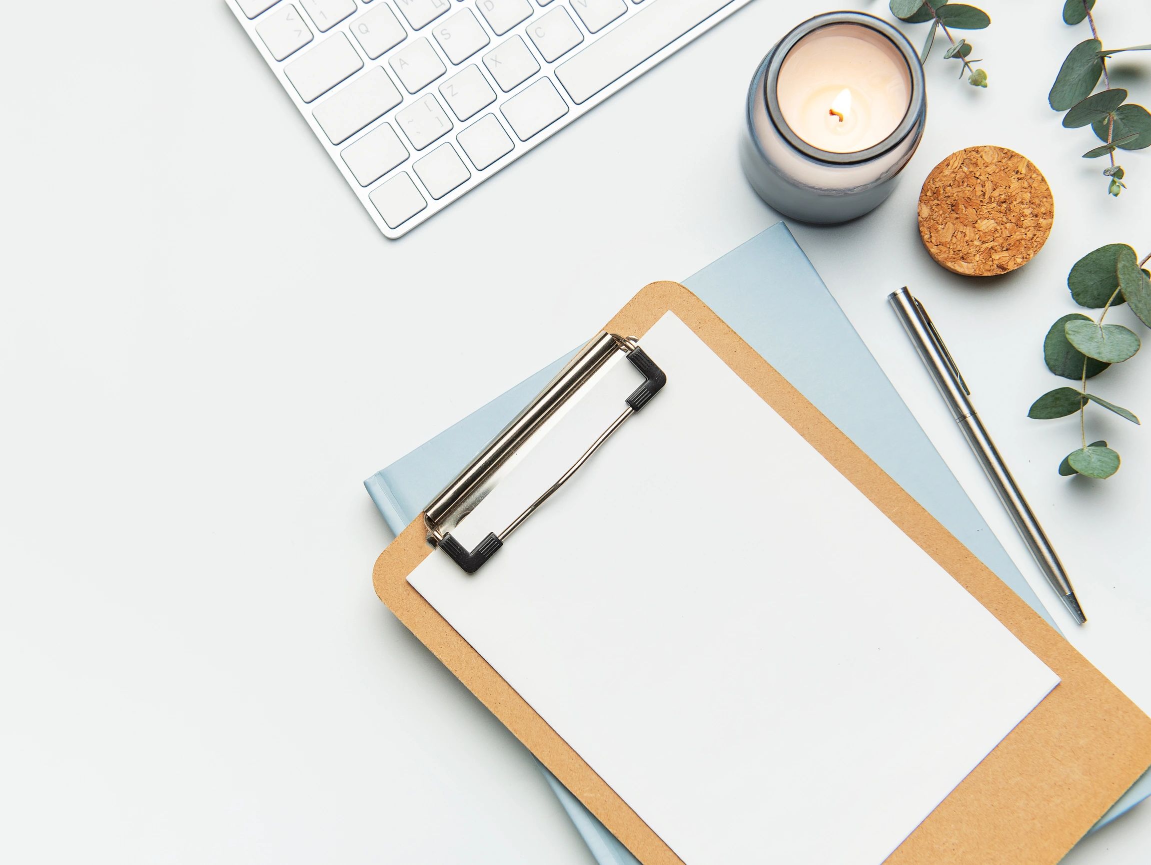 Minimalist workspace with clipboard, candle, pen, and keyboard.