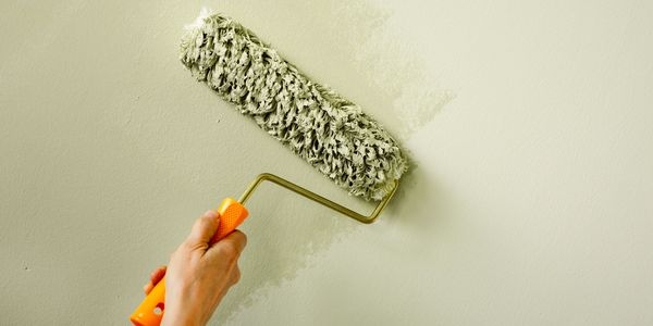 Hand painting a wall with a roller brush in light green.