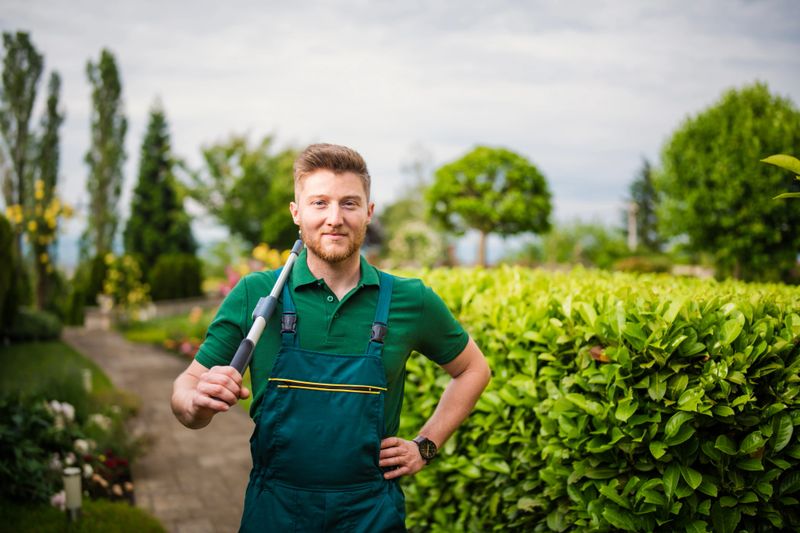 Portrait of a cheerful and smiling young landscaper at work in a beautiful green garden holding hedge clippers.