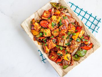 Colorful stir-fried tofu with bell peppers and green onions on a rustic plate.