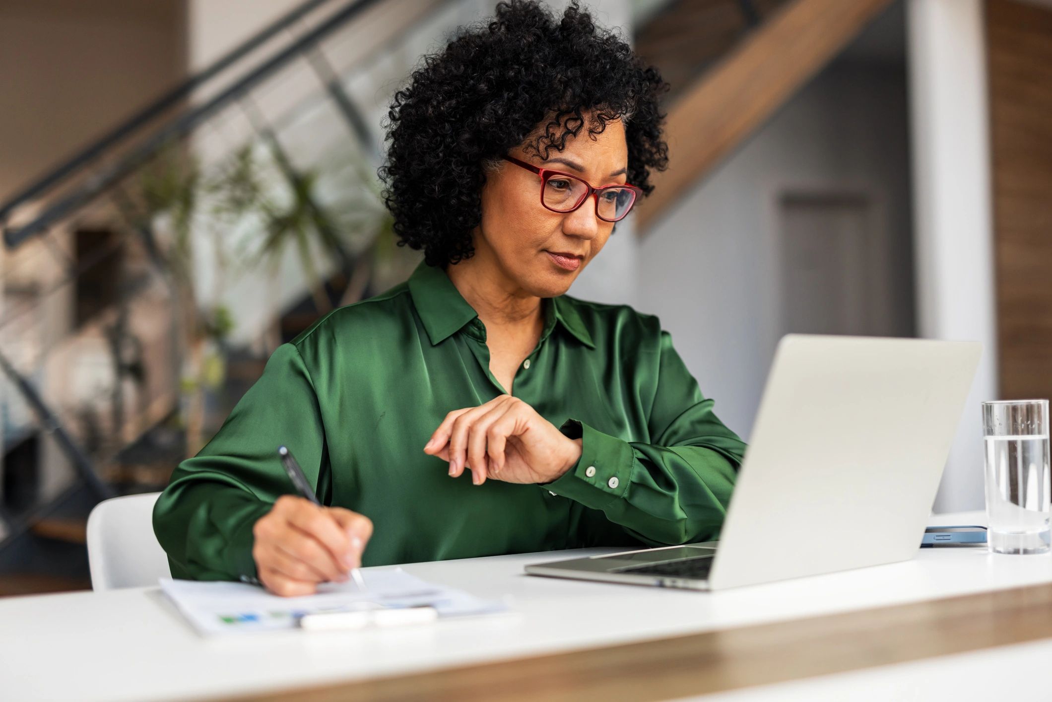 Smiling professional taking notes at a desk with a laptop in a bright office
