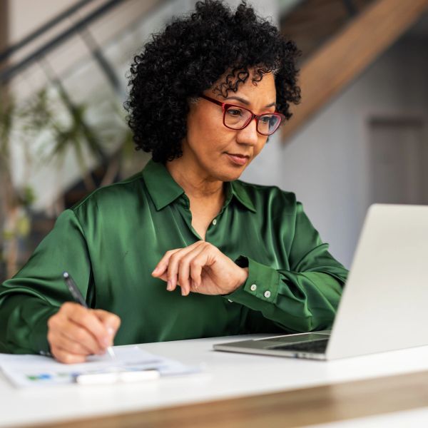 Woman working on laptop and writing notes.