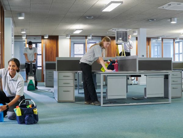 Janitorial staff cleaning a modern office with desks and partitions.