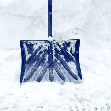 Blue snow shovel stuck in fresh white snow.