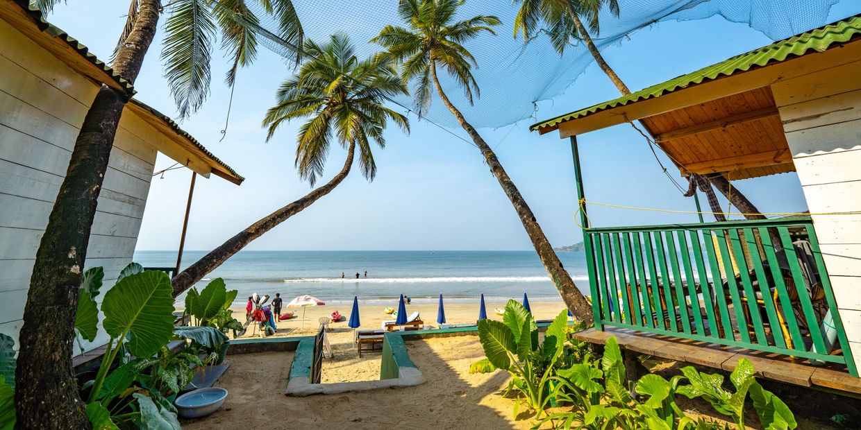 Palm trees and beach huts frame a sunny tropical beach scene.