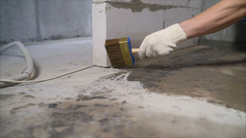 Construction worker waterproofing concrete floor using a brush, ensuring protection against moisture and enhancing durability