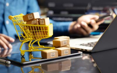 Miniature shopping cart with packages on a tablet.